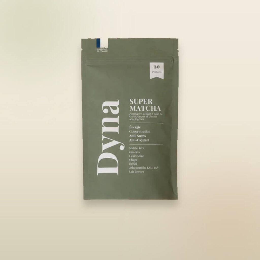 Sachet vert mat de Super Matcha Dyna présenté sur un fond beige clair. L’emballage indique 30 portions et met en avant une alternative au café à base de matcha, champignons et plantes adaptogènes. Les bénéfices affichés incluent énergie, concentration, anti-stress et antioxydant, avec des ingrédients comme le matcha bio, le guarana, le Lion’s Mane, le chaga, le reishi, l’ashwagandha KSM-66® et le lait de coco.